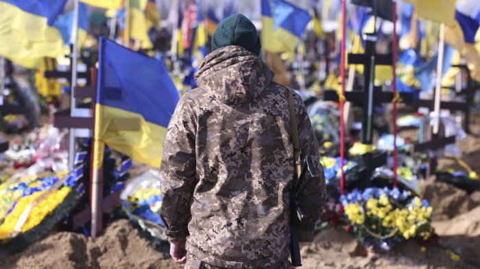 A Ukrainian soldier stands in front of the graves of Ukrainian soldiers killed in the war at a cemetery in Kharkiv.
